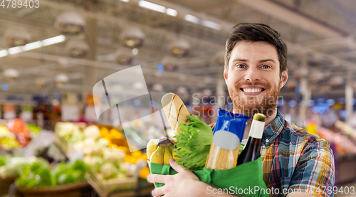 Image of smiling young man with food in bag at supermarket