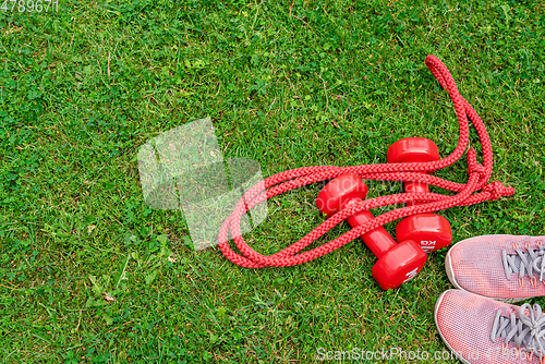 Image of Ladie's dumbbles and sneakers on the green grass background