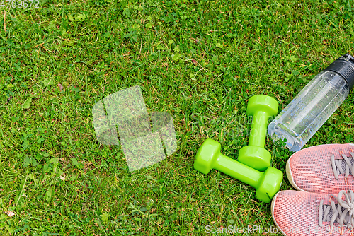 Image of Ladie's dumbbles and sneakers on the green grass background