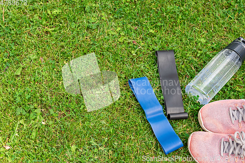 Image of Ladie's fitness rubber bands and sneakers on the green grass background