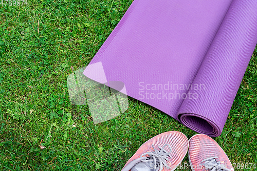 Image of Ladie's sneakers and fitness mat on the green grass background