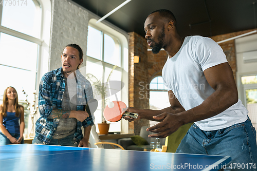 Image of Young people playing table tennis in workplace, having fun