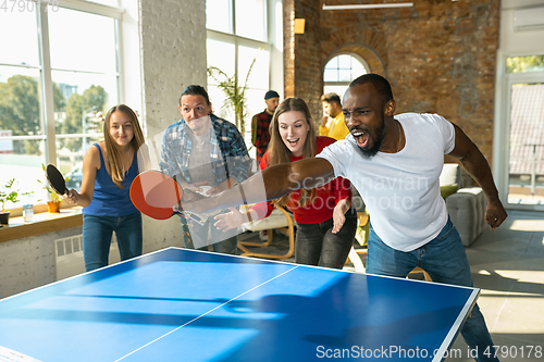 Image of Young people playing table tennis in workplace, having fun