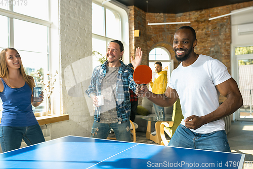 Image of Young people playing table tennis in workplace, having fun