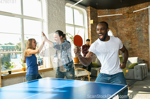 Image of Young people playing table tennis in workplace, having fun