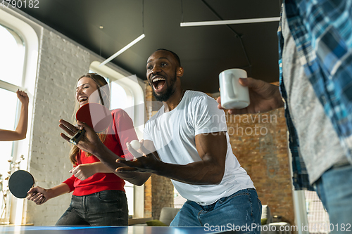 Image of Young people playing table tennis in workplace, having fun