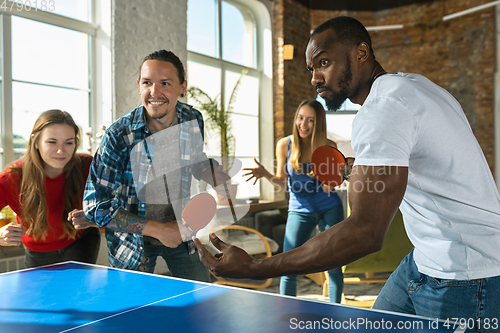 Image of Young people playing table tennis in workplace, having fun