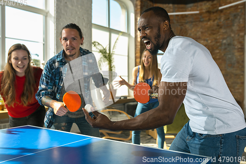 Image of Young people playing table tennis in workplace, having fun