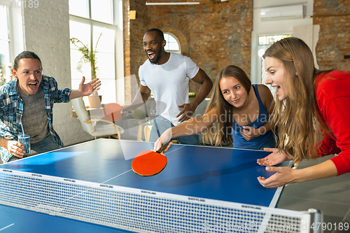 Image of Young people playing table tennis in workplace, having fun