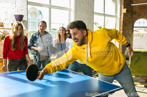 Image of Young people playing table tennis in workplace, having fun