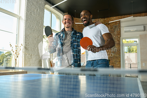 Image of Young men playing table tennis in workplace, having fun