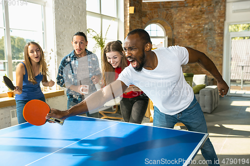 Image of Young people playing table tennis in workplace, having fun