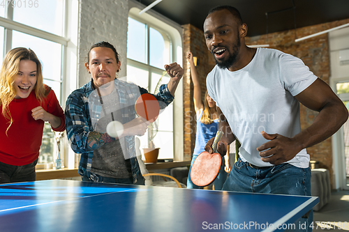 Image of Young people playing table tennis in workplace, having fun