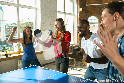 Image of Young people playing table tennis in workplace, having fun