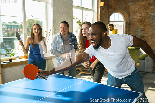 Image of Young people playing table tennis in workplace, having fun