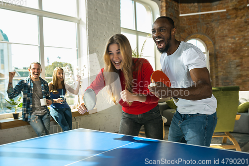 Image of Young people playing table tennis in workplace, having fun