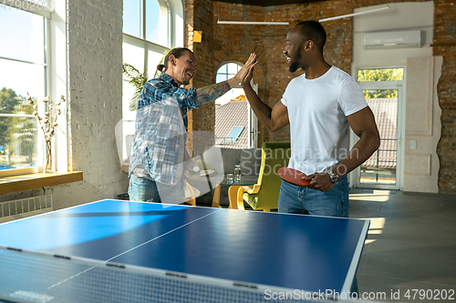 Image of Young men playing table tennis in workplace, having fun