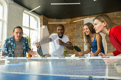 Image of Young people playing table tennis in workplace, having fun