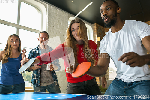 Image of Young people playing table tennis in workplace, having fun