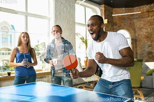 Image of Young people playing table tennis in workplace, having fun