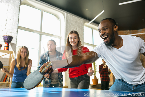 Image of Young people playing table tennis in workplace, having fun