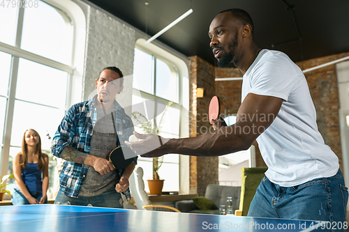 Image of Young people playing table tennis in workplace, having fun