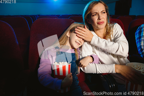 Image of Young caucasian mother and daughter watching a film at a movie theater