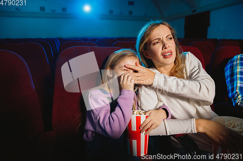 Image of Young caucasian mother and daughter watching a film at a movie theater