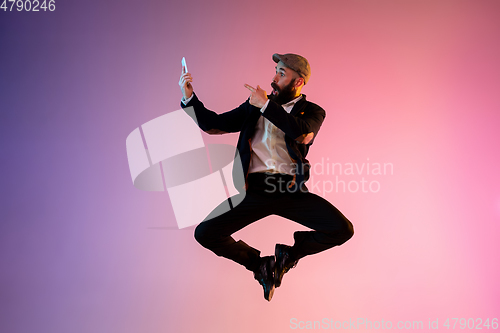 Image of Full length portrait of happy jumping man in neon light and gradient background