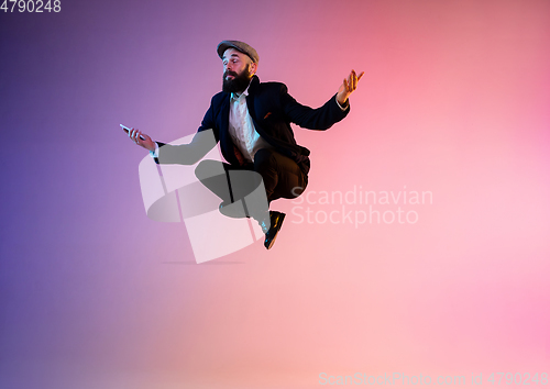 Image of Full length portrait of happy jumping man in neon light and gradient background