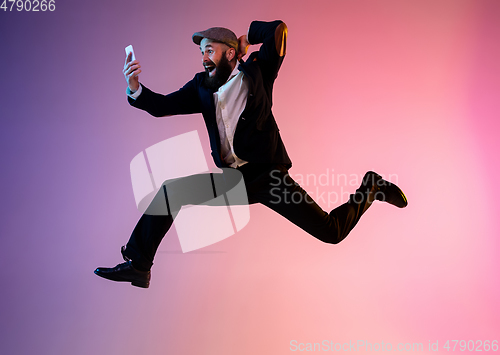 Image of Full length portrait of happy jumping man in neon light and gradient background