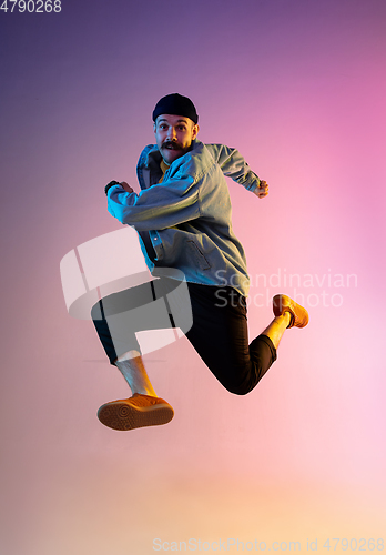 Image of Full length portrait of happy jumping man in neon light and gradient background