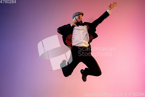 Image of Full length portrait of happy jumping man in neon light and gradient background