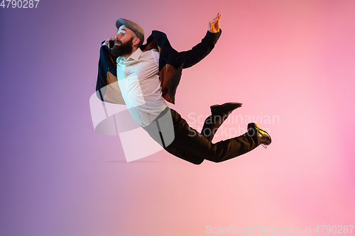 Image of Full length portrait of happy jumping man in neon light and gradient background