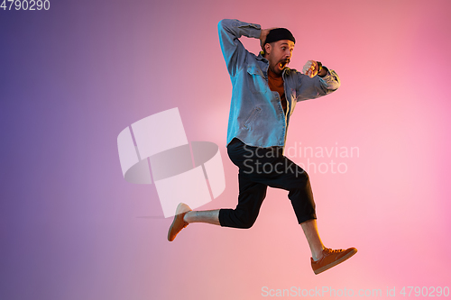 Image of Full length portrait of happy jumping man in neon light and gradient background