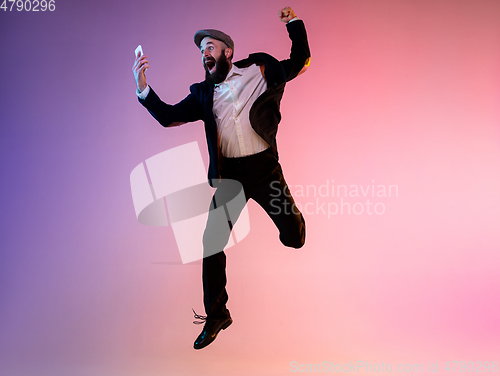 Image of Full length portrait of happy jumping man in neon light and gradient background