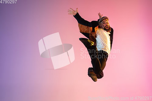 Image of Full length portrait of happy jumping man in neon light and gradient background