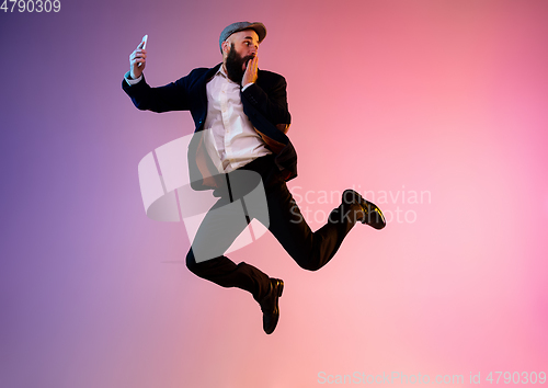 Image of Full length portrait of happy jumping man in neon light and gradient background