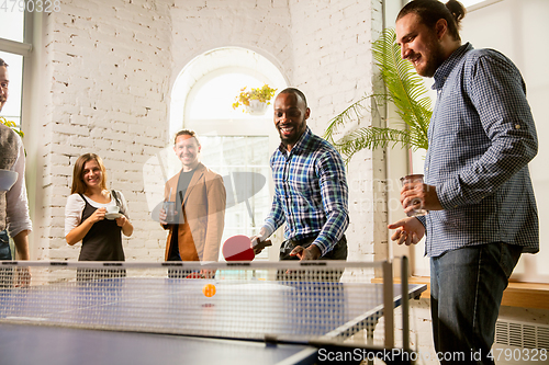 Image of Young people playing table tennis in workplace, having fun