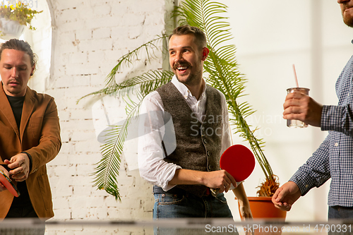 Image of Young people playing table tennis in workplace, having fun