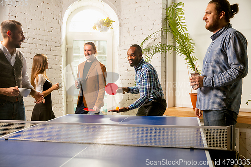 Image of Young people playing table tennis in workplace, having fun