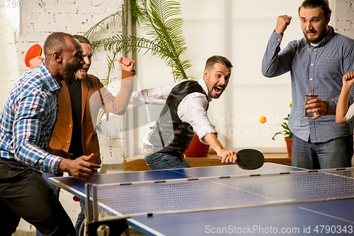 Image of Young people playing table tennis in workplace, having fun