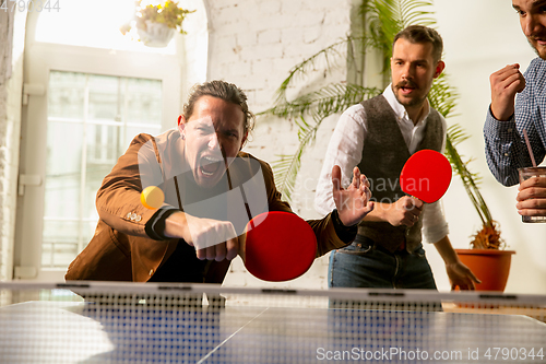 Image of Young people playing table tennis in workplace, having fun