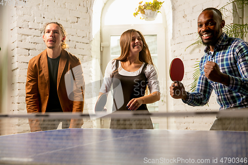 Image of Young people playing table tennis in workplace, having fun