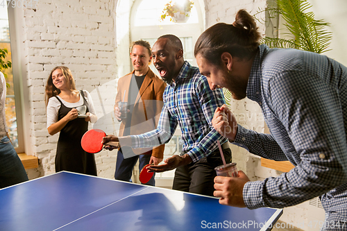 Image of Young people playing table tennis in workplace, having fun