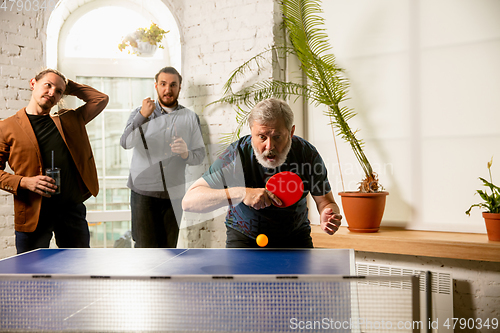 Image of Young people playing table tennis in workplace, having fun