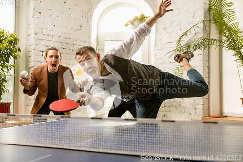 Image of Young people playing table tennis in workplace, having fun