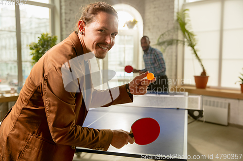 Image of Young men playing table tennis in workplace, having fun