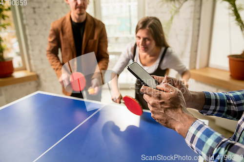 Image of Young people playing table tennis in workplace, having fun