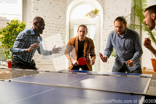 Image of Young people playing table tennis in workplace, having fun